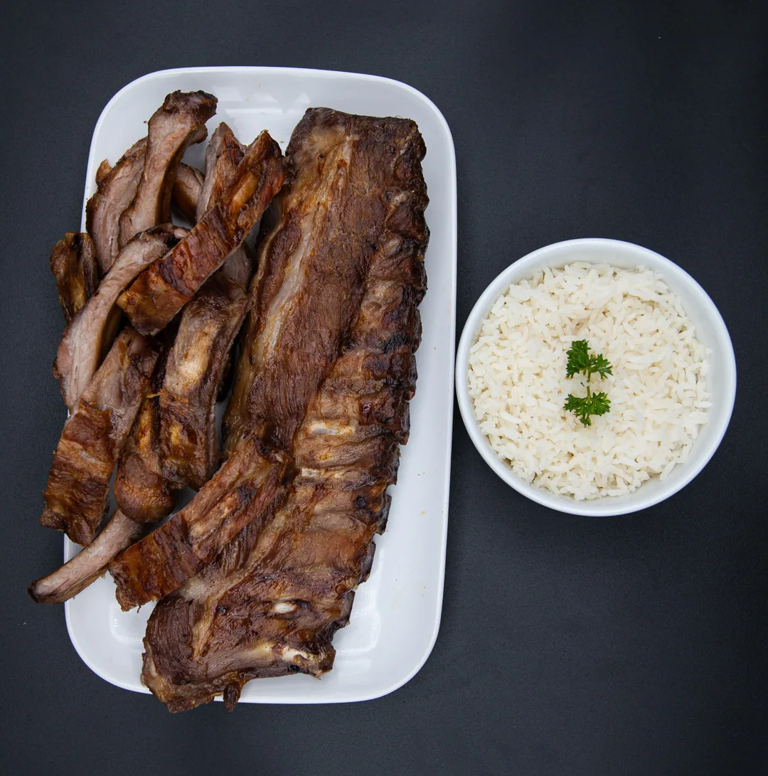 Costelinha de porco grelhada no churrasco, com uma tigela de arroz branco ao lado