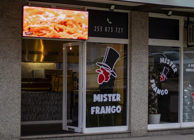 Fachada do Mister Frango em Braga, com o letreiro e o telefone no vidro da montra